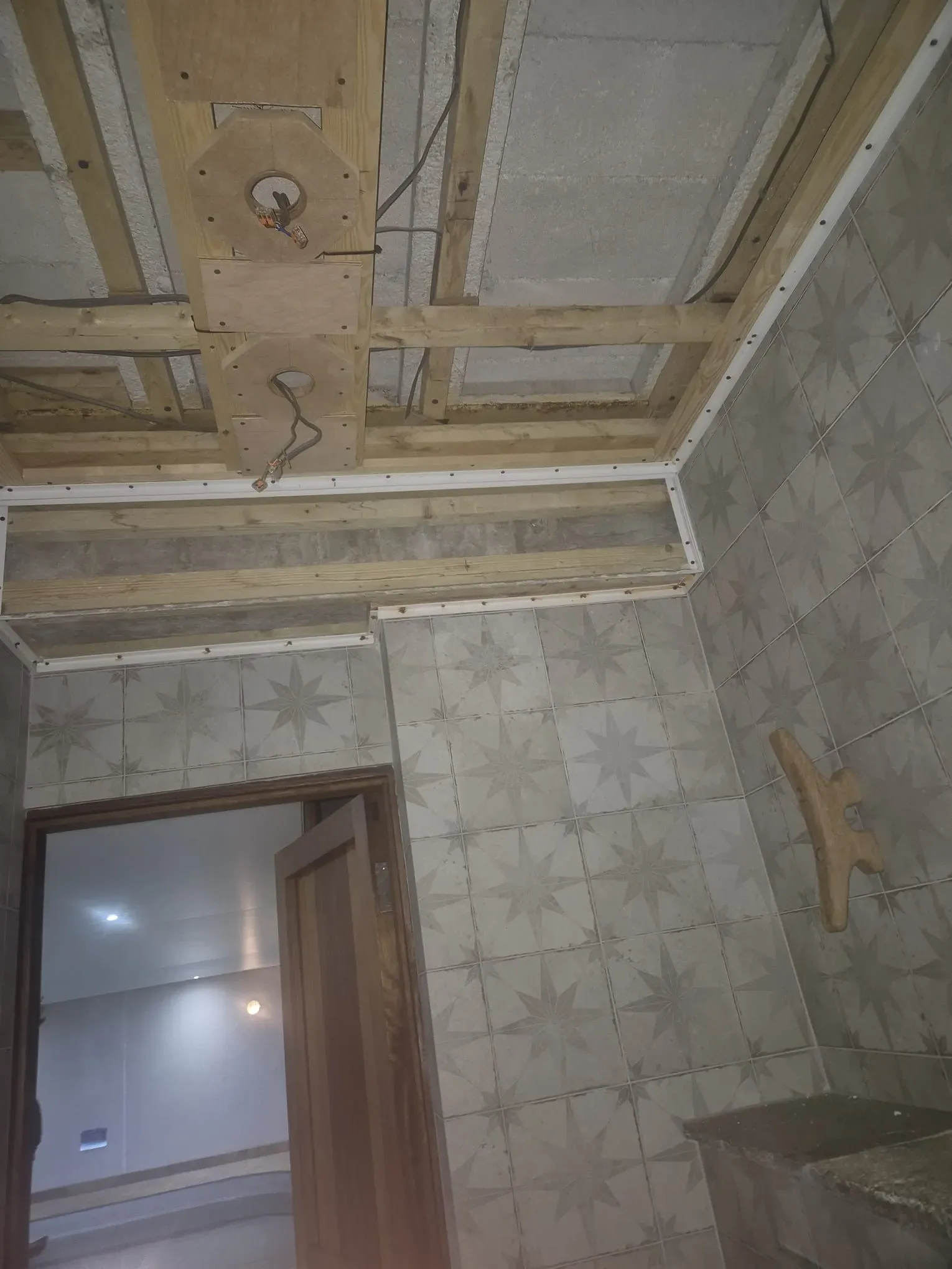 Interior room under renovation with exposed ceiling joists, electrical wiring, and decorative grey wall tiles, showing ongoing building work.