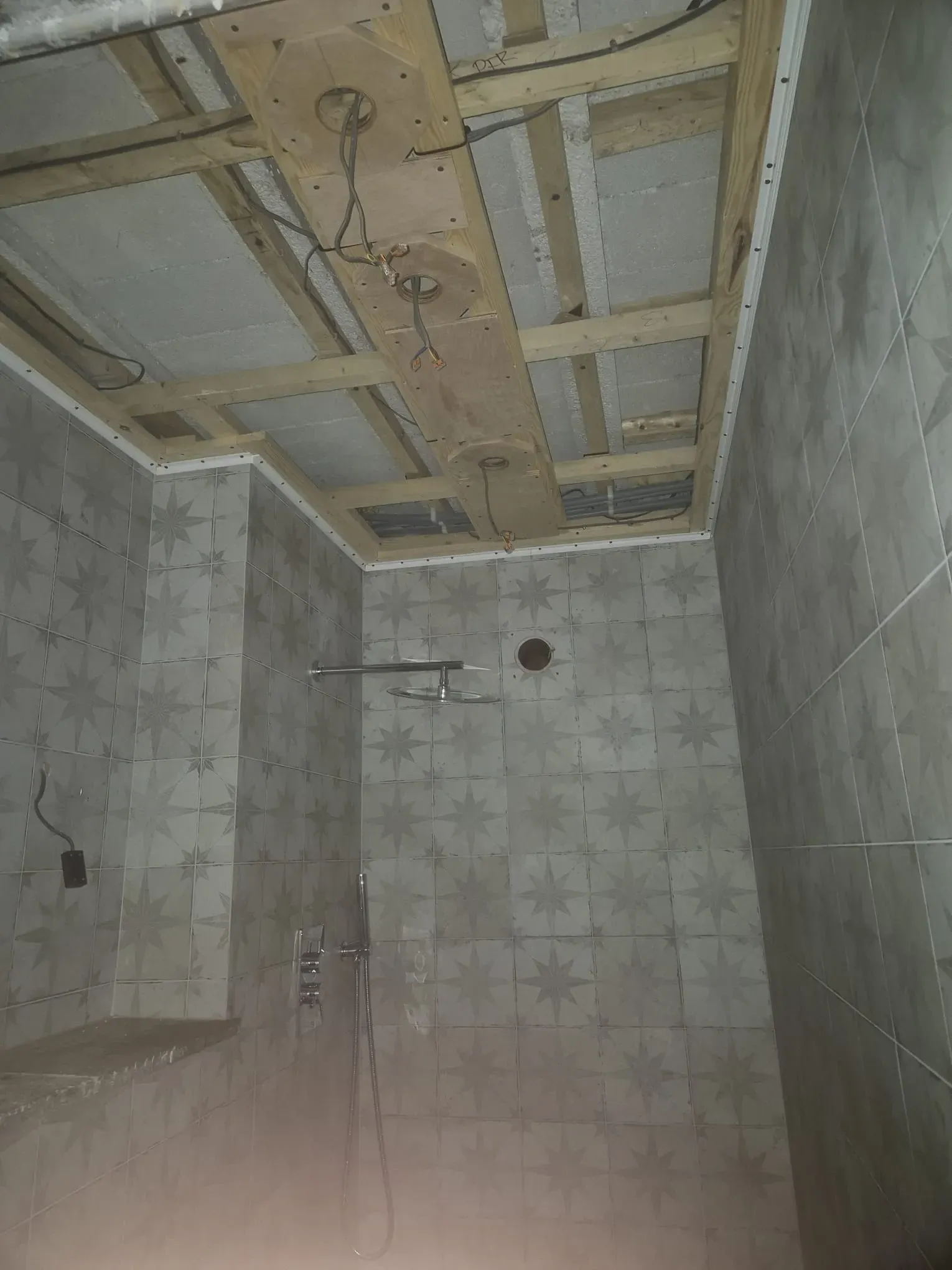 Bathroom refurbishment underway, displaying star-patterned tiled walls, exposed ceiling joists, and hanging electrical cables.