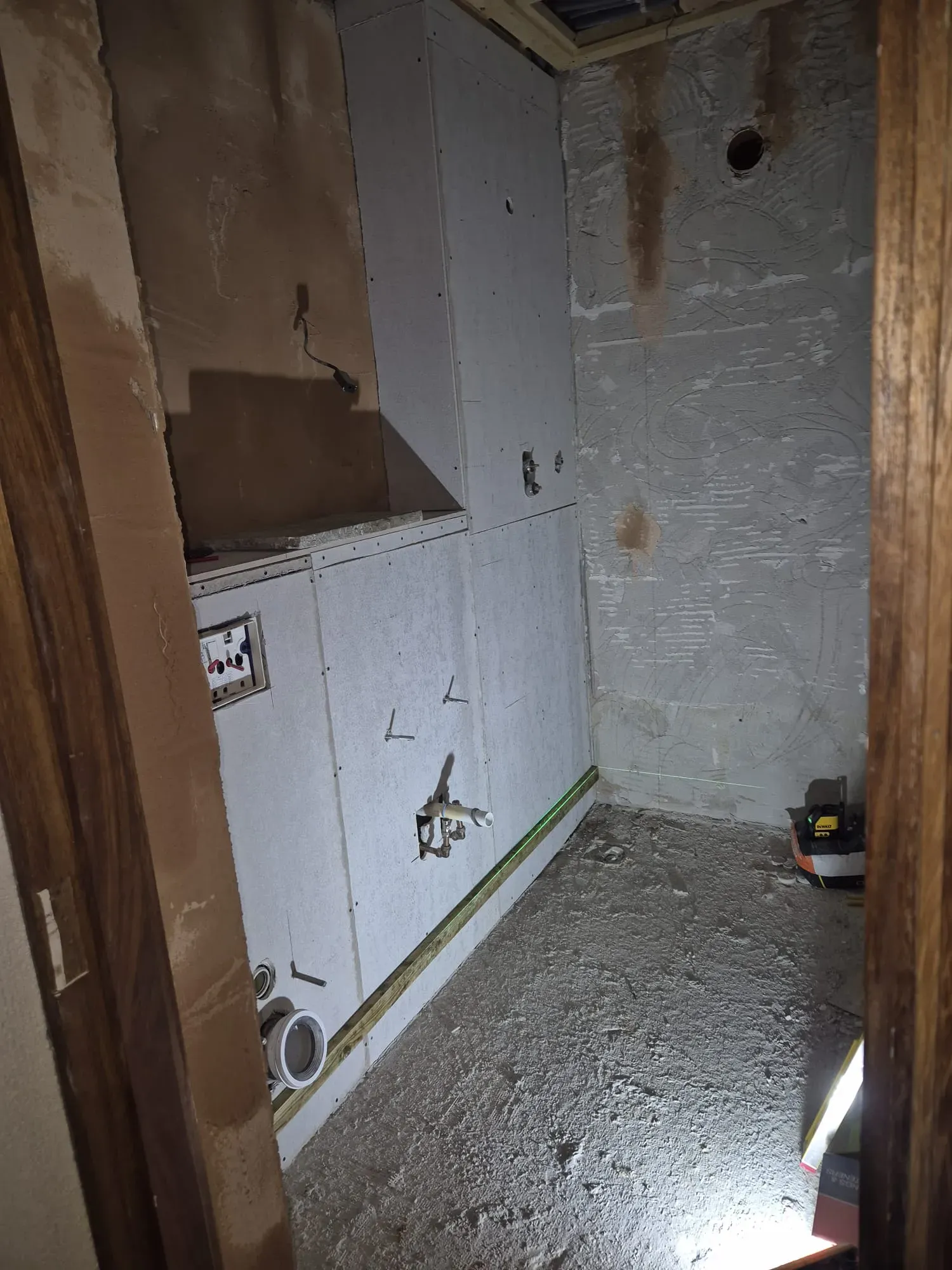 Room interior under renovation with plasterboard walls, exposed pipes, and electrical wiring, ready for tiling or decoration.